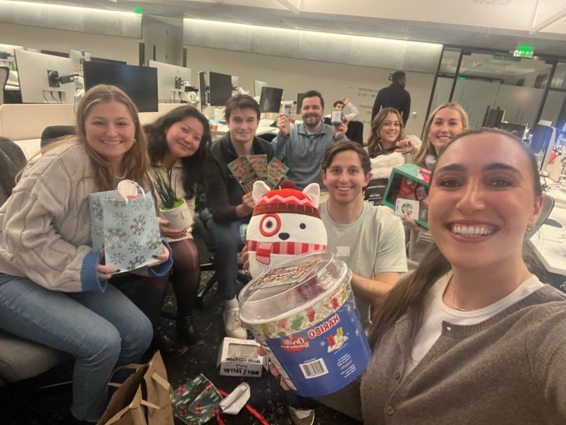 Taylor Chinitz and her teammates pose for a photo while holding holiday gifts in the office